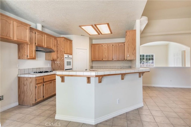 11471 Azure View Rd, Pinon Hills, CA 92372 - kitchen with white oven, tile countertops, gas stovetop, a breakfast bar area, and light tile patterned flooring