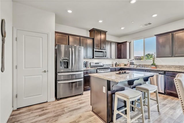 2146 N Rinaldi Ct, Visalia, CA 93291 - kitchen featuring stainless steel appliances, dark brown cabinets, light stone counters, a breakfast bar, and a kitchen island