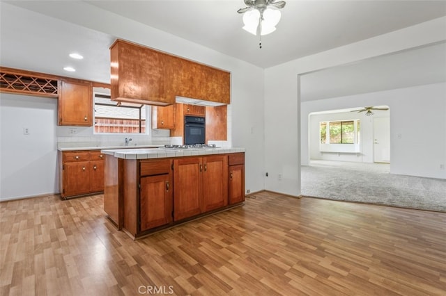 9726 Kimberly Ave, Montclair, CA 91763 - kitchen featuring a ceiling fan, black oven, brown cabinetry, light wood-style flooring, and tile counters
