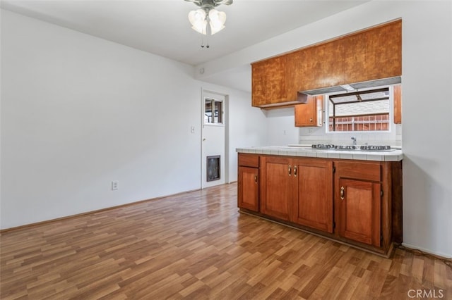 9726 Kimberly Ave, Montclair, CA 91763 - kitchen featuring stainless steel gas stovetop, light wood-type flooring, ceiling fan, tile counters, and brown cabinets
