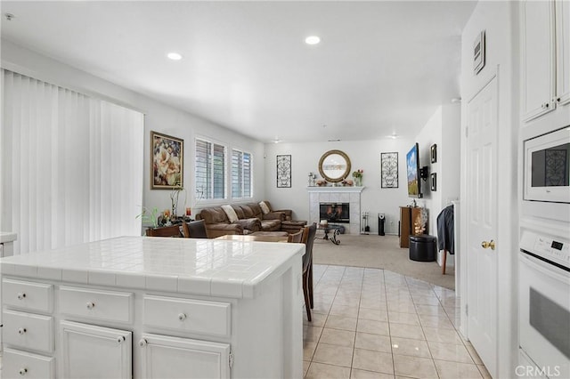 15029 Coyote Ct, Fontana, CA 92336 - kitchen featuring tile counters, white appliances, a tile fireplace, white cabinets, and light colored carpet