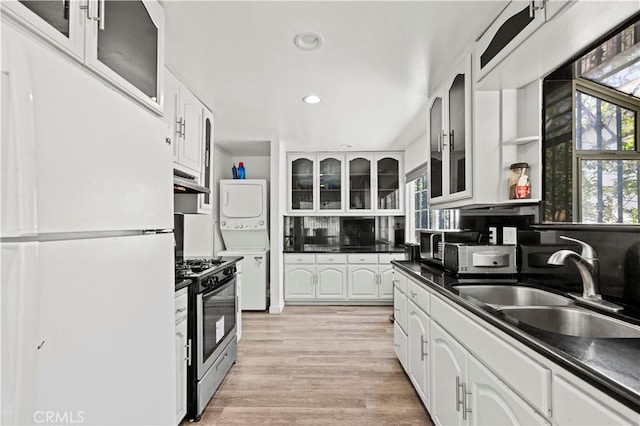 12616 Terra Bella St, Pacoima, CA 91331 - kitchen with freestanding refrigerator, stainless steel gas range, stacked washer and clothes dryer, dark countertops, and white cabinets