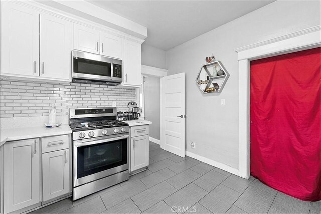 1665 Arlington Ave, Los Angeles, CA 90019 - kitchen featuring appliances with stainless steel finishes, light countertops, backsplash, white cabinetry, and light tile patterned floors