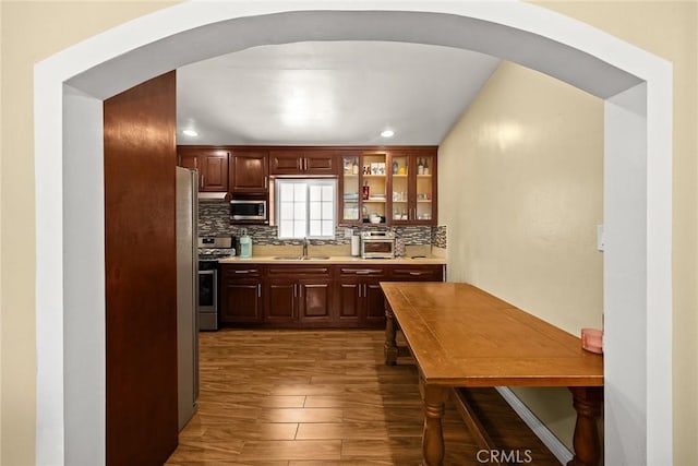 13162 Oaks Ave, Chino, CA 91710 - kitchen featuring appliances with stainless steel finishes, arched walkways, dark wood-style floors, light countertops, and backsplash