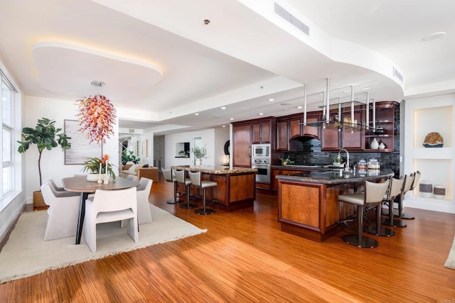 1325 Pacific Hwy Unit 3403, San Diego, CA 92101 - kitchen featuring stainless steel appliances, a kitchen breakfast bar, wood finished floors, tasteful backsplash, and wall chimney exhaust hood