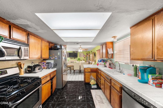 14134 Orizaba Ave, Paramount, CA 90723 - kitchen featuring appliances with stainless steel finishes, tile counters, a ceiling fan, and brown cabinets