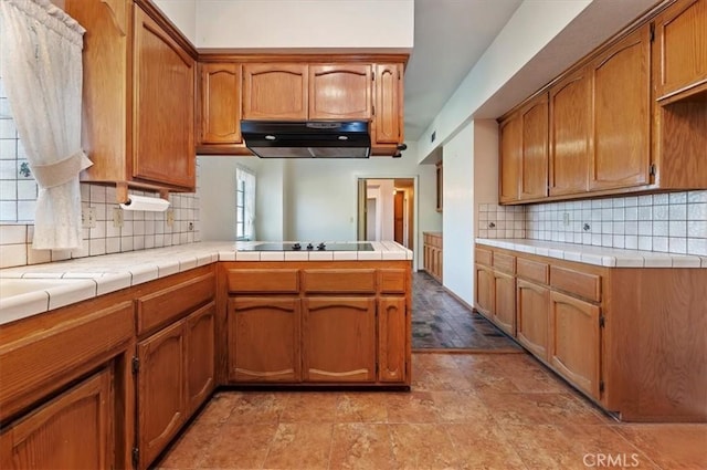 29801 Maxine Ln, Menifee, CA 92584 - kitchen with under cabinet range hood, black electric stovetop, a peninsula, brown cabinets, and decorative backsplash