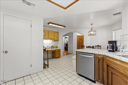22820 Mariposa Rd, Tehachapi, CA 93561 - kitchen with stainless steel dishwasher, arched walkways, brown cabinetry, tile counters, and decorative light fixtures