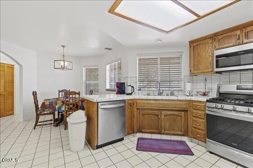 22820 Mariposa Rd, Tehachapi, CA 93561 - kitchen featuring stainless steel appliances, backsplash, brown cabinetry, arched walkways, and pendant lighting