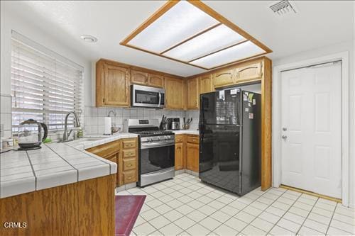 22820 Mariposa Rd, Tehachapi, CA 93561 - kitchen with appliances with stainless steel finishes, tile counters, tasteful backsplash, light tile patterned floors, and brown cabinets