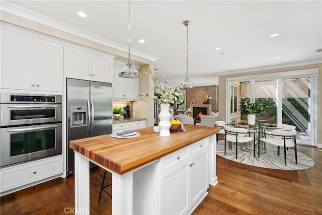 32 Tesoro, Irvine, CA 92618 - kitchen featuring appliances with stainless steel finishes, wooden counters, white cabinetry, a large fireplace, and pendant lighting