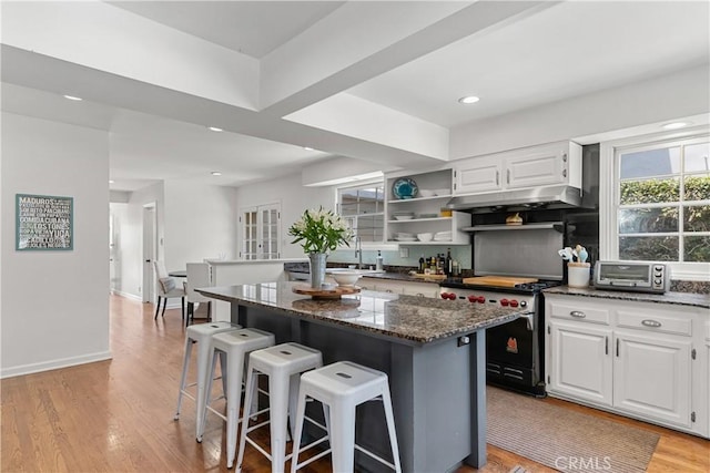 1733 Bayou Way, Seal Beach, CA 90740 - kitchen with stainless steel range oven, a breakfast bar, under cabinet range hood, dark stone counters, and a kitchen island