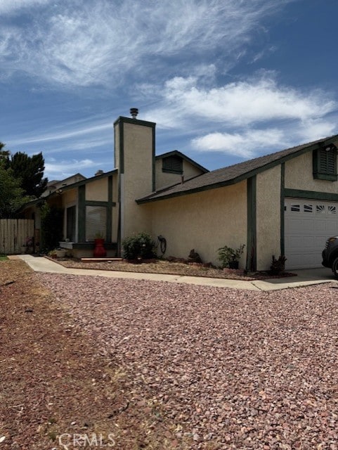 12446 Mount Baldy Dr, Victorville, CA 92392 - view of side of home with stucco siding, a garage, and a chimney
