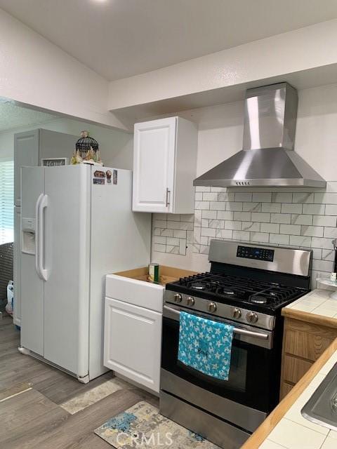 12446 Mount Baldy Dr, Victorville, CA 92392 - kitchen featuring stainless steel gas range, wall chimney range hood, white refrigerator with ice dispenser, tile counters, and light wood-style flooring