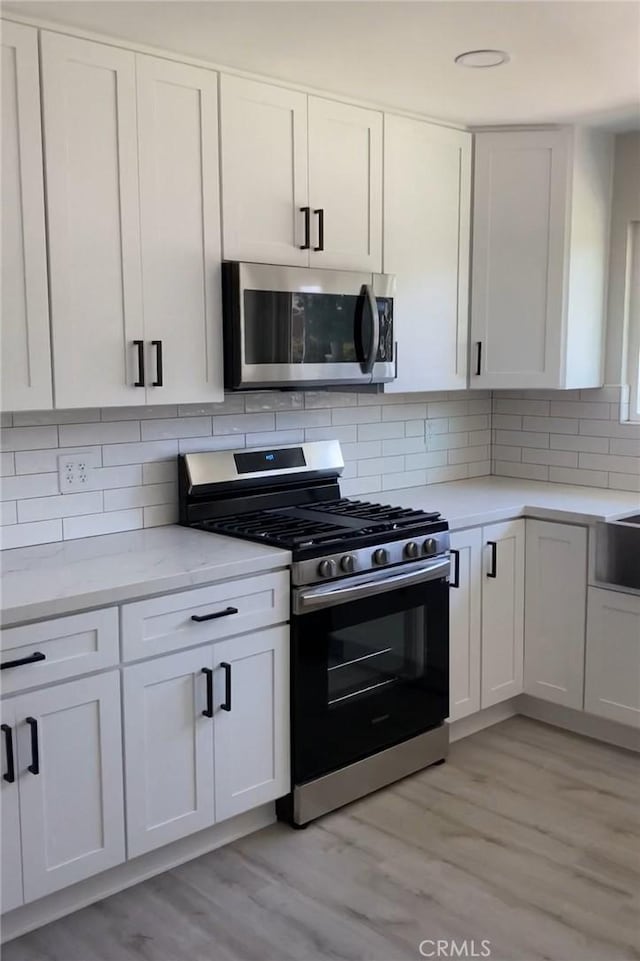 3195 Camarillo Ave, Oceanside, CA 92056 - kitchen with stainless steel appliances, light wood-style floors, white cabinetry, tasteful backsplash, and light stone counters