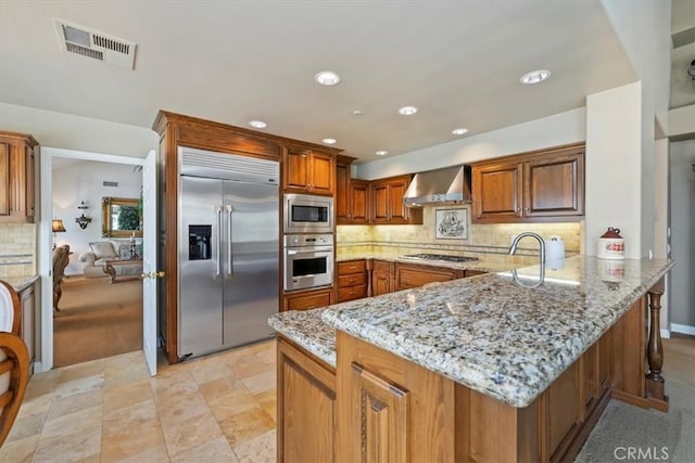 10847 Leota Ln, Riverside, CA 92503 - kitchen featuring built in appliances, wall chimney range hood, a peninsula, light stone counters, and decorative backsplash