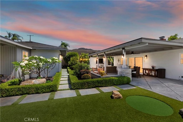 1335 N Vallejo Way, Upland, CA 91786 - back of house at dusk featuring a patio, a putting green, an outdoor living space, a lawn, and stucco siding