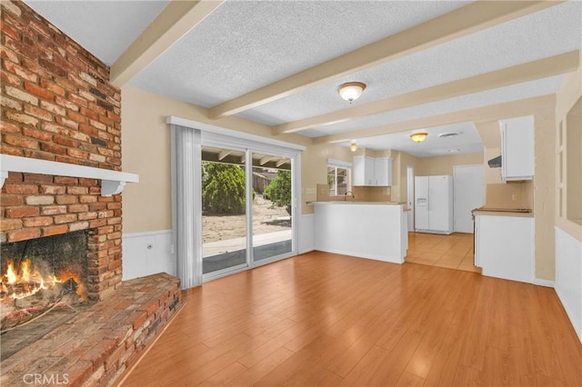 20468 College Blvd, Riverside, CA 92507 - unfurnished living room with beamed ceiling, a fireplace, a textured ceiling, light wood-type flooring, and wainscoting