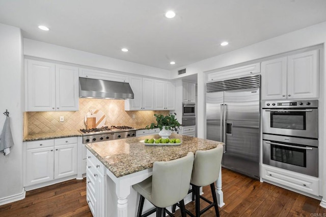 3474 Camino Cereza, Carlsbad, CA 92009 - kitchen featuring stainless steel appliances, exhaust hood, dark wood-style floors, light stone countertops, and a breakfast bar