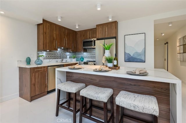 100 Scholz Plz Unit 205, Newport Beach, CA 92663 - kitchen featuring appliances with stainless steel finishes, light countertops, a kitchen island, decorative backsplash, and a breakfast bar area