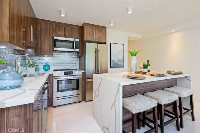 100 Scholz Plz Unit 205, Newport Beach, CA 92663 - kitchen with stainless steel appliances, decorative backsplash, a breakfast bar area, light stone countertops, and a kitchen island