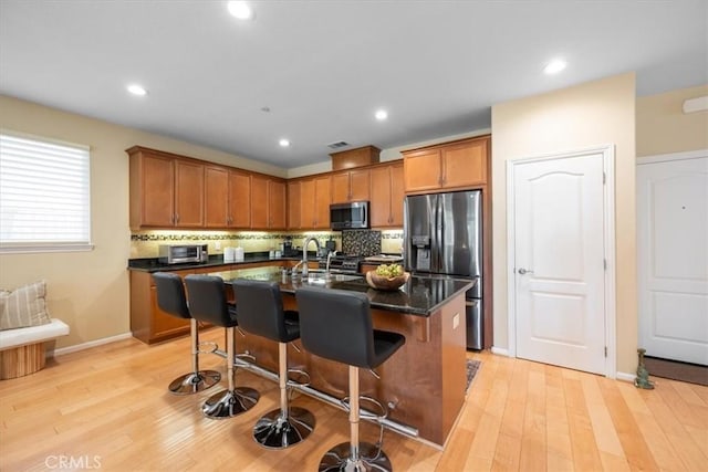 1061 Ford Dr, Nipomo, CA 93444 - kitchen featuring appliances with stainless steel finishes, brown cabinetry, a kitchen breakfast bar, decorative backsplash, and light wood-type flooring