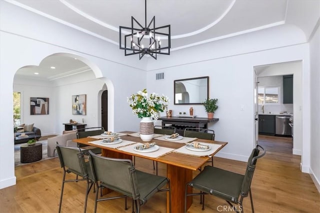 4325 9th Ave, Los Angeles, CA 90008 - dining space featuring arched walkways, light wood finished floors, a chandelier, and a raised ceiling