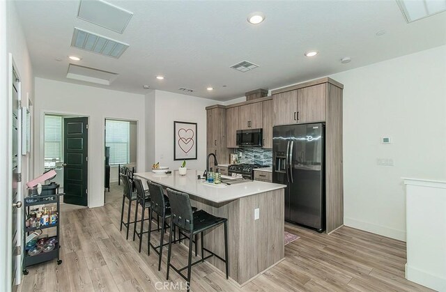 2887 E Tamarind Dr, Fresno, CA 93730 - kitchen featuring refrigerator with ice dispenser, a breakfast bar, a kitchen island with sink, light wood-style flooring, and recessed lighting