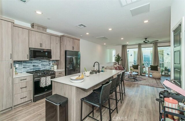 2887 E Tamarind Dr, Fresno, CA 93730 - kitchen featuring appliances with stainless steel finishes, a kitchen bar, open floor plan, light brown cabinets, and light wood-style floors