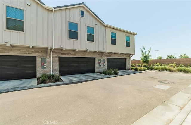 2887 E Tamarind Dr, Fresno, CA 93730 - view of front of home with board and batten siding, a garage, stone siding, and driveway