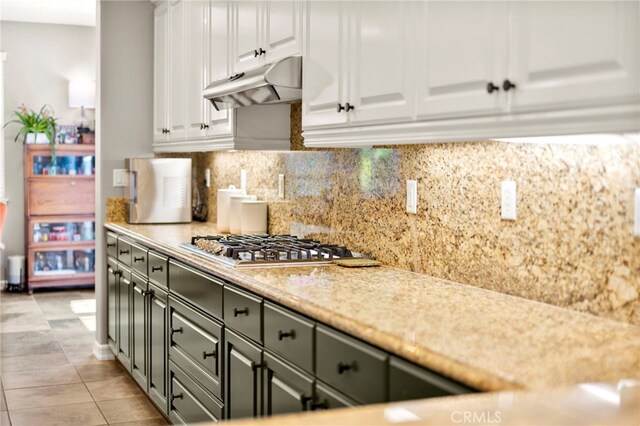46287 Durango Dr, Temecula, CA 92592 - kitchen with under cabinet range hood, white cabinetry, stainless steel gas stovetop, backsplash, and light tile patterned flooring