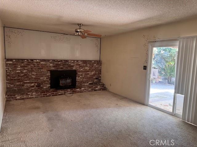 3246 Shamrock Ave, Merced, CA 95340 - unfurnished living room featuring carpet, a textured ceiling, ceiling fan, and a wood stove