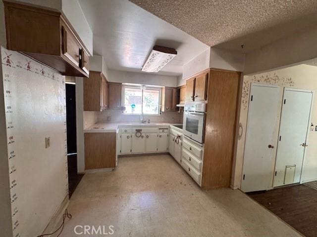 3246 Shamrock Ave, Merced, CA 95340 - kitchen with white oven, light countertops, light flooring, decorative backsplash, and brown cabinets