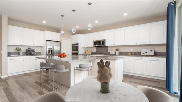 5120 Armendarez Ln, Fontana, CA 92336 - kitchen with appliances with stainless steel finishes, white cabinetry, light wood-style flooring, a breakfast bar area, and recessed lighting