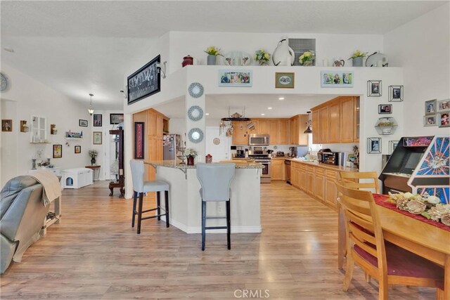 26460 Gem Ct, Helendale, CA 92342 - kitchen featuring appliances with stainless steel finishes, a kitchen breakfast bar, light wood-type flooring, light stone counters, and open floor plan