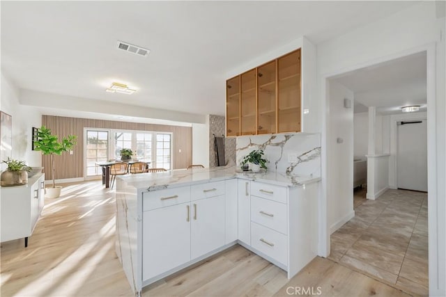 24135 Las Naranjas Dr, Laguna Niguel, CA 92677 - kitchen with a peninsula, light stone countertops, backsplash, white cabinetry, and light wood-type flooring