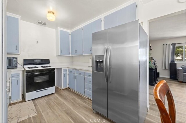 1022 E Lancaster Blvd, Lancaster, CA 93535 - kitchen featuring white gas range oven, stainless steel fridge with ice dispenser, blue cabinets, light countertops, and light wood-type flooring