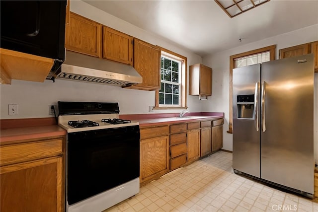 707 Marin St, Corning, CA 96021 - kitchen with stainless steel fridge, gas stove, under cabinet range hood, light countertops, and brown cabinets