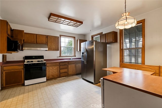 707 Marin St, Corning, CA 96021 - kitchen featuring white gas stove, under cabinet range hood, stainless steel refrigerator with ice dispenser, black microwave, and hanging light fixtures