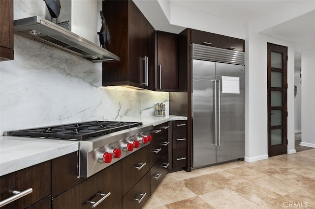 5390 Carlsbad Blvd, Carlsbad, CA 92008 - kitchen featuring appliances with stainless steel finishes, wall chimney range hood, backsplash, dark brown cabinetry, and light stone counters