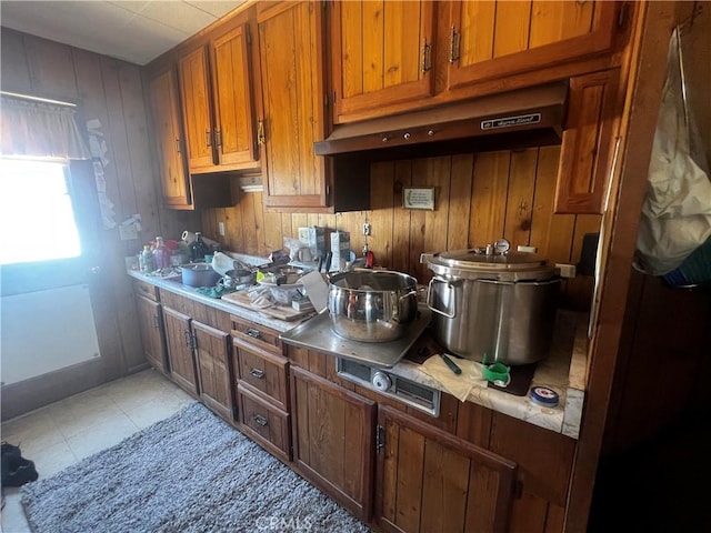 1489 Balsa Ave, Yucca Valley, CA 92284 - kitchen featuring under cabinet range hood, brown cabinetry, light countertops, wooden walls, and light tile patterned floors