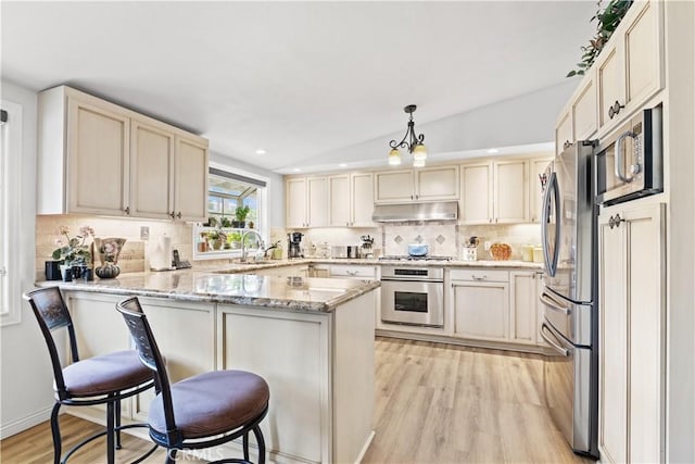 14091 Dall Ln, Tustin, CA 92780 - kitchen featuring appliances with stainless steel finishes, under cabinet range hood, a peninsula, light wood-style flooring, and a kitchen bar