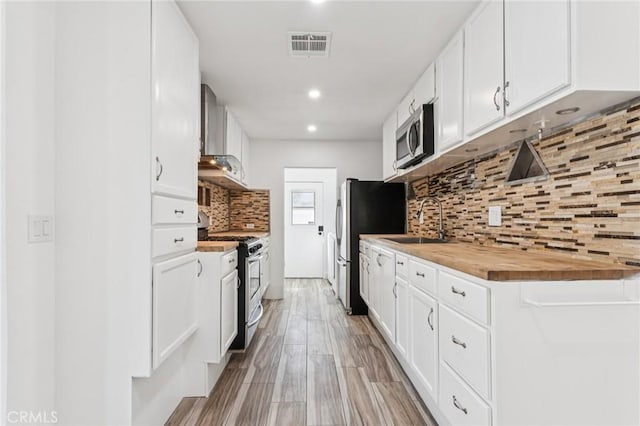 38876 Foxholm Dr, Palmdale, CA 93551 - kitchen featuring stainless steel appliances, wall chimney range hood, backsplash, wood counters, and white cabinetry