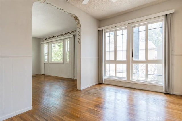 15300 Mayall St, San Fernando, CA 91345 - spare room with wood finished floors, a wainscoted wall, a textured ceiling, a ceiling fan, and arched walkways