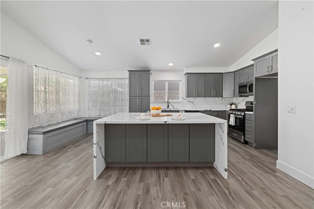 3624 Comet Ct, Palmdale, CA 93550 - kitchen with stainless steel appliances, vaulted ceiling, gray cabinetry, a center island, and light wood-type flooring