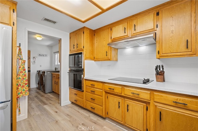 7009 Etter St, Bakersfield, CA 93308 - kitchen with black appliances, under cabinet range hood, washer and clothes dryer, light wood-style flooring, and light countertops
