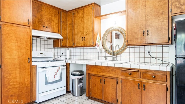 480 W D St, Colton, CA 92324 - kitchen featuring under cabinet range hood, white gas stove, decorative backsplash, light tile patterned floors, and freestanding refrigerator