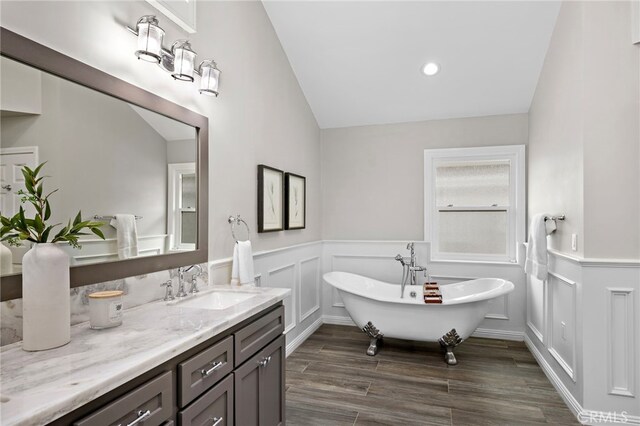 609 Calle Reata, San Clemente, CA 92673 - bathroom featuring wood finished floors, vaulted ceiling, vanity, a freestanding bath, and a wainscoted wall