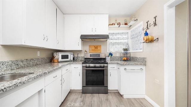 2648 N G St, San Bernardino, CA 92405 - kitchen with stainless steel range with gas stovetop, under cabinet range hood, white microwave, white cabinets, and light wood finished floors