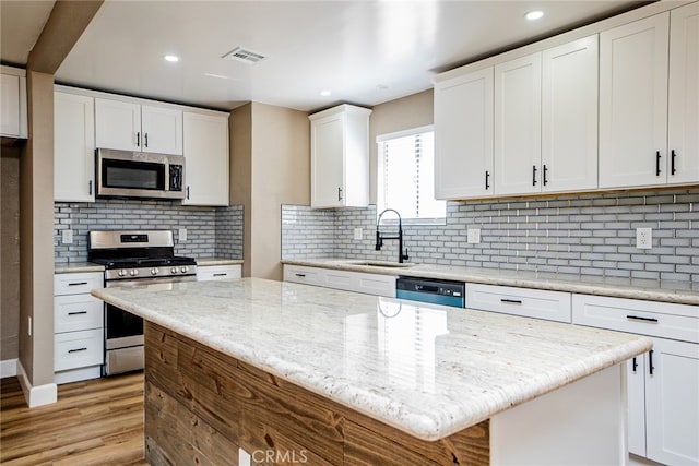 73570 Cedar Dr Unit 29, Palms, CA 92277 - kitchen with stainless steel appliances, white cabinetry, light wood-style flooring, a kitchen island, and backsplash